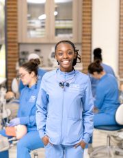 Dental student in scrubs smiling at camera in lab.