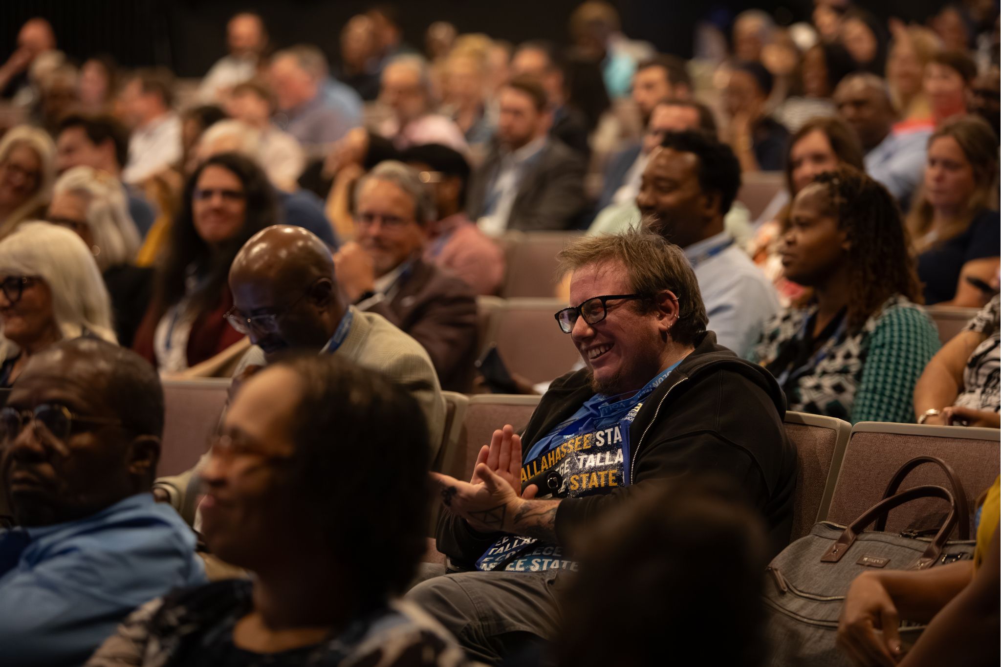 Summit attendees in auditorium seats clapping.