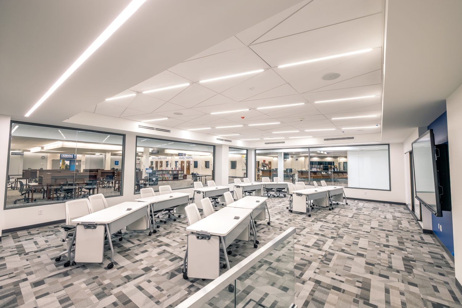 Empty classroom with white desks and large screen.