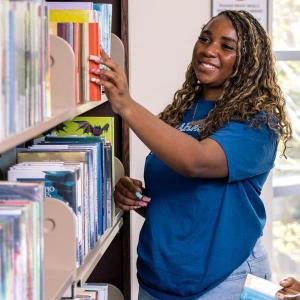 Student pulling book from library shelf.