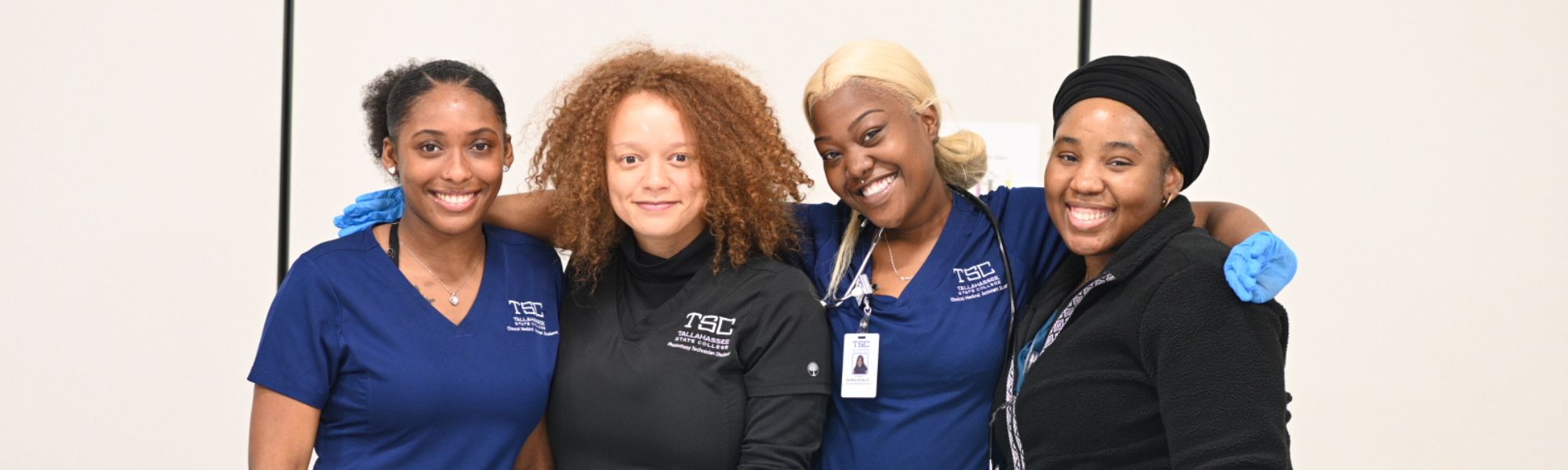 Four healthcare students wearing scrubs and smiling at the camera.